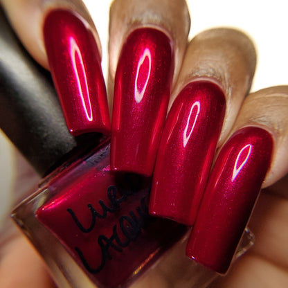 Red nail polish bottle with nails painted red held by a hand